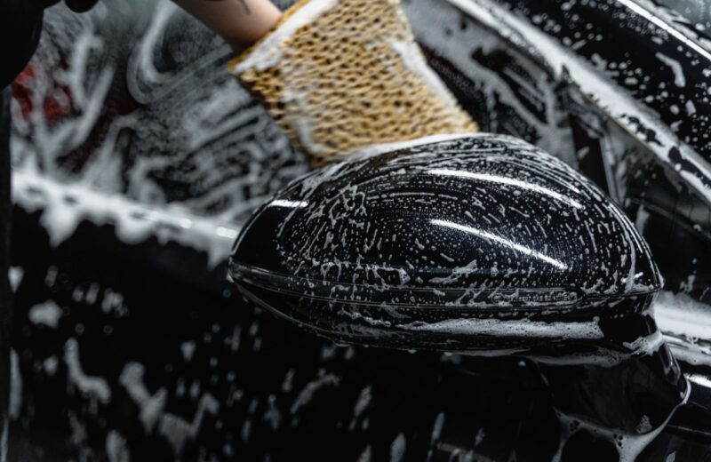 A wash mitt with foam on a black wing mirror