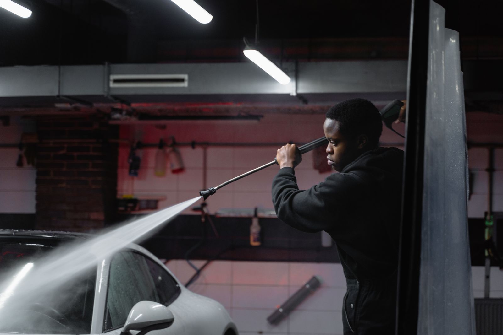 A detailer rinsing a car with a pressure washer in an indoor bay