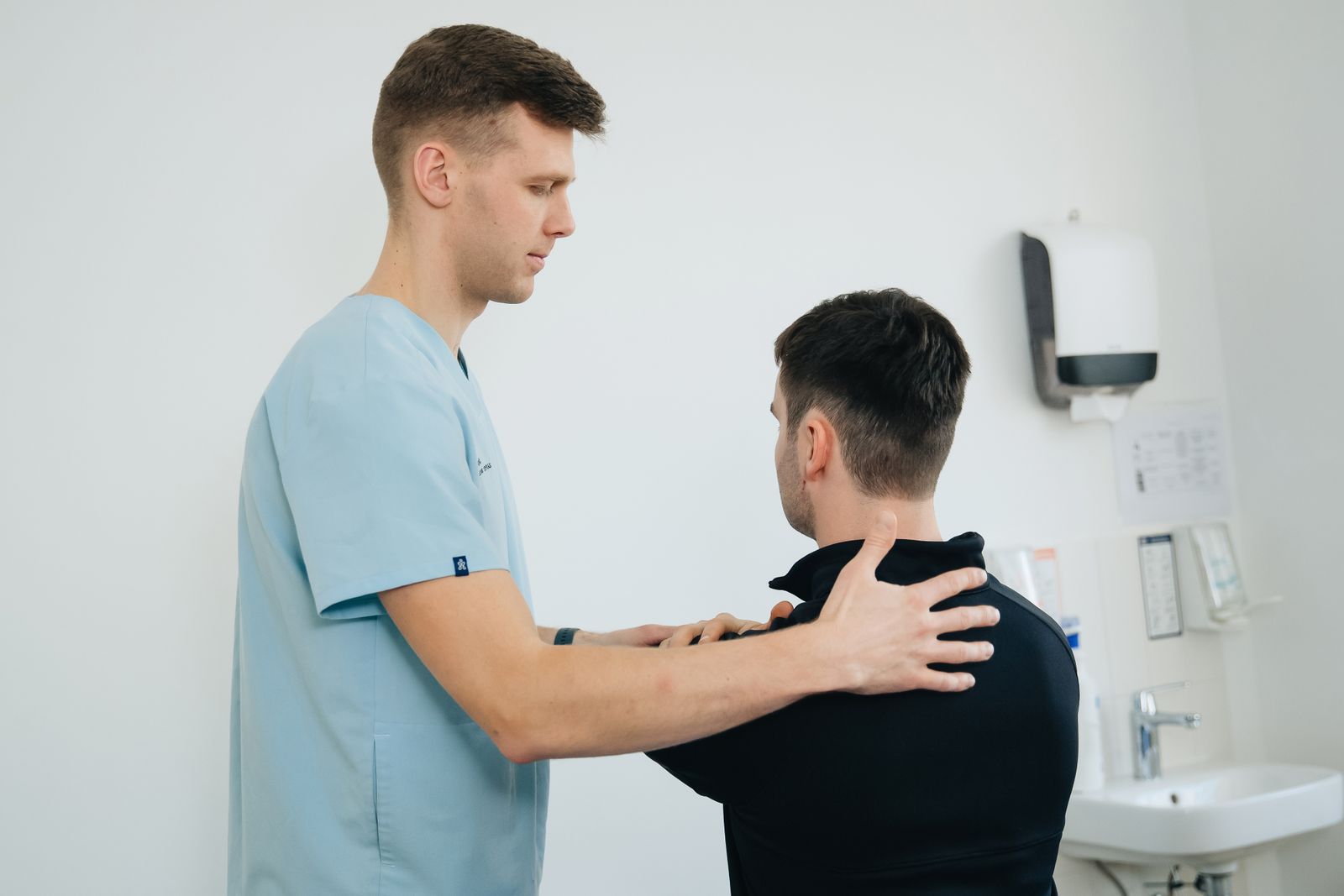 A physiotherapist checking a patient's shoulder in a bright treatment room