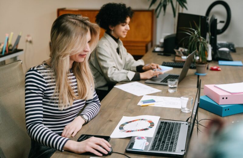 Two colleagues comparing figures on their laptops in an office