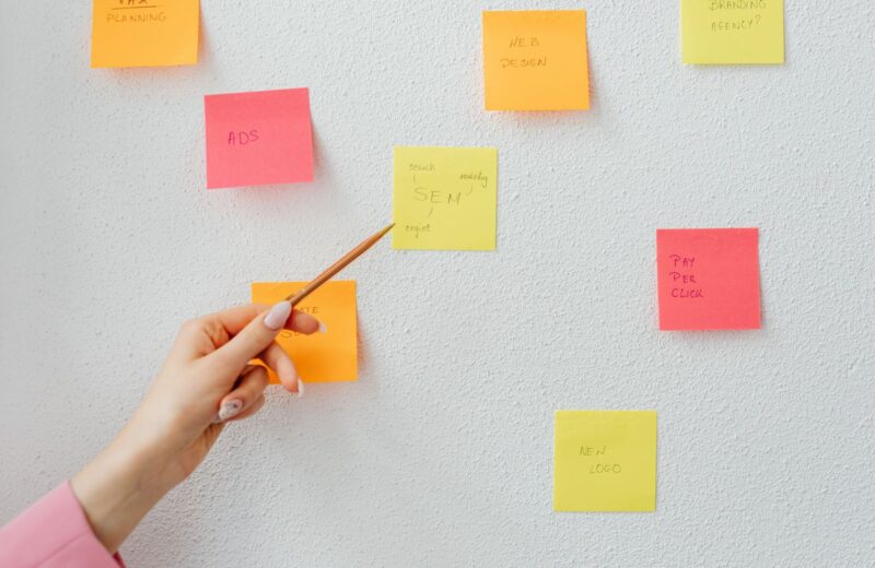 A hand pointing at coloured sticky notes on a white wall