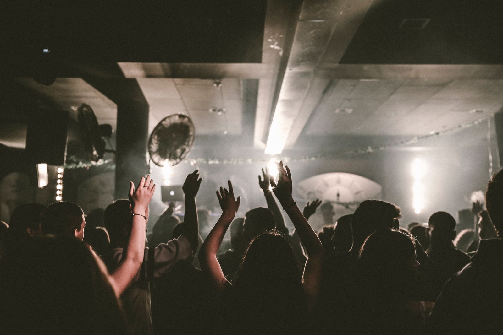 A packed dance floor seen from behind, hands up under an arched concrete ceiling