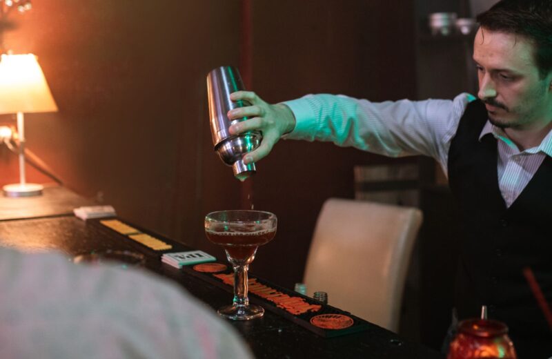 A bartender pouring a drink from a shaker into a glass
