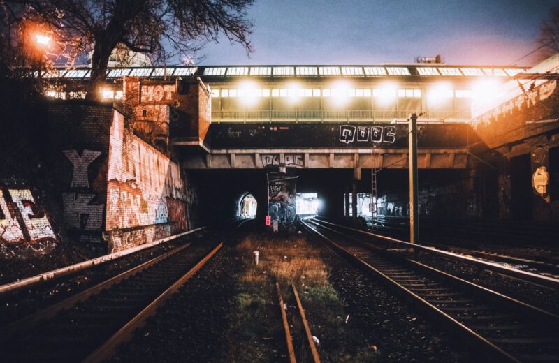 Railway tracks running under a lit bridge at night