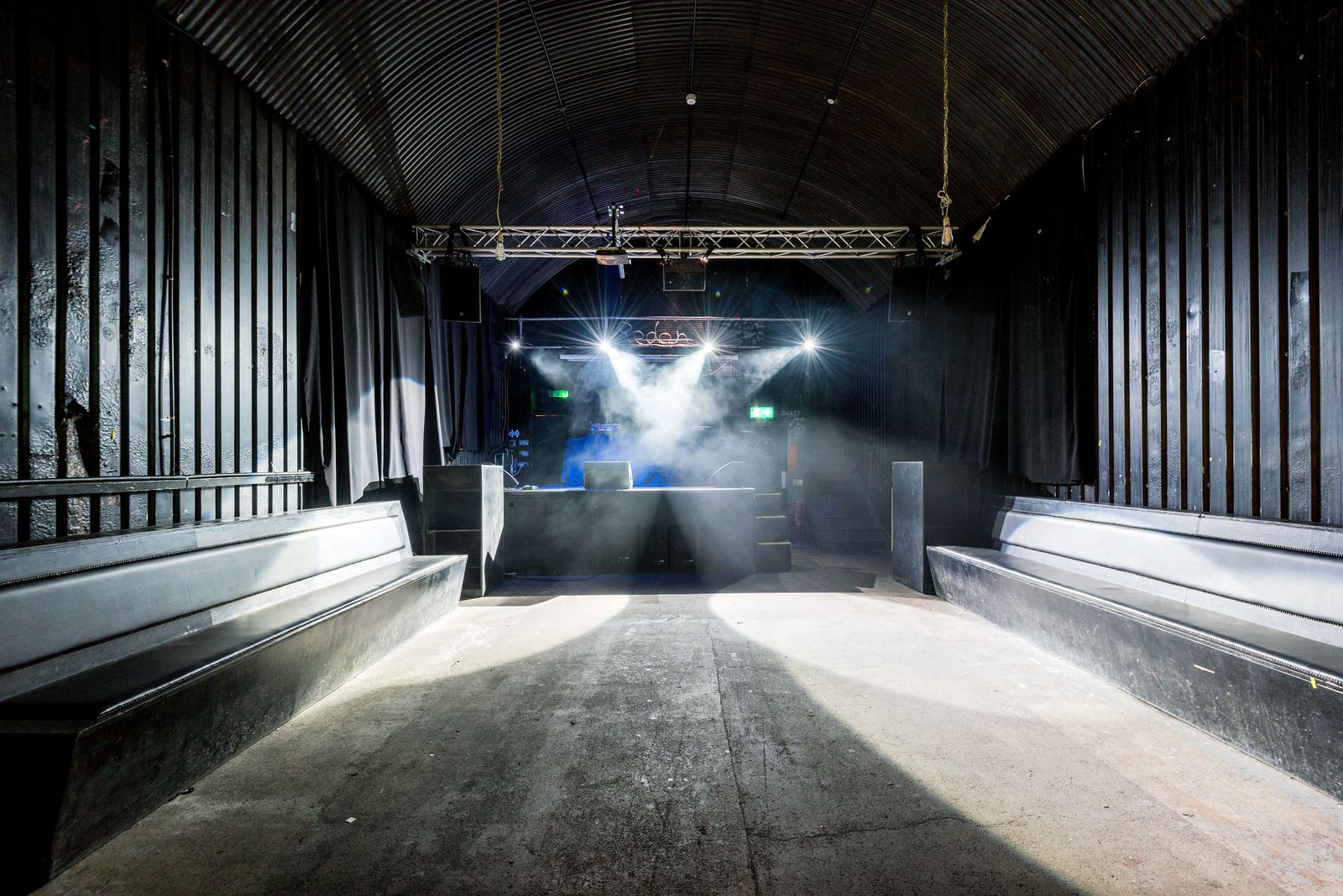 The empty club under a curved roof, stage lights and haze over the booth at the far end