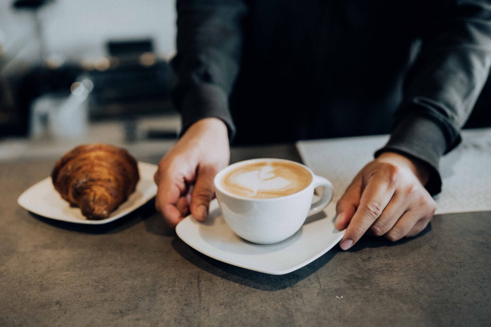 A latte and a croissant set down on a café counter
