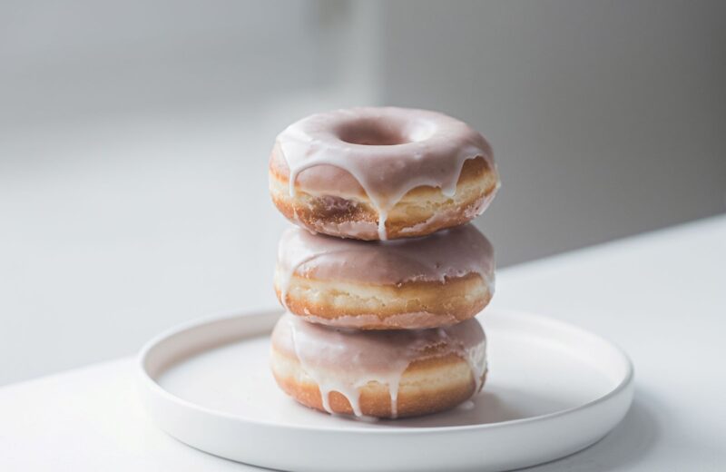 Three glazed donuts stacked on a white plate