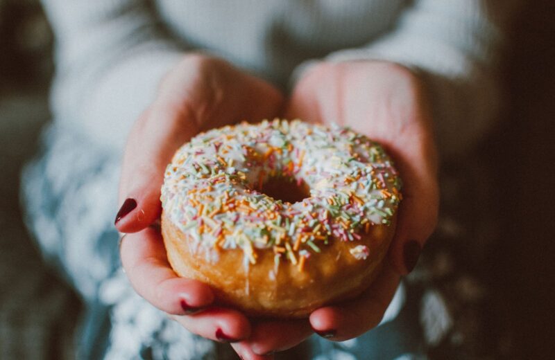A donut with coloured sprinkles held in two hands