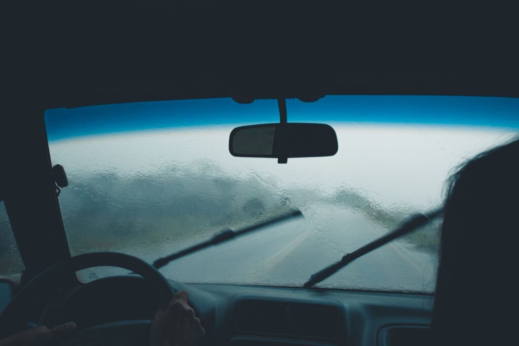 Rain on a car windscreen with the wipers moving over a wet road ahead