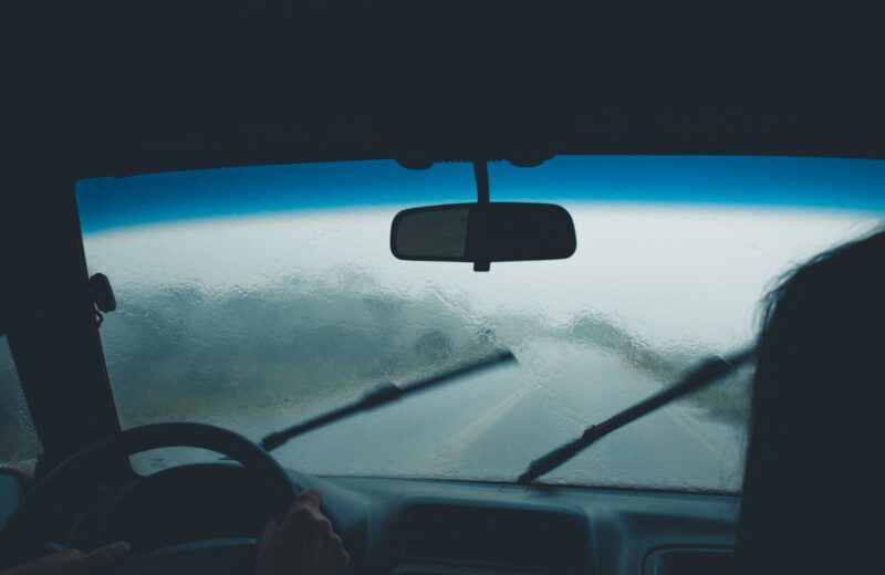 Rain on a car windscreen with the wipers moving over a wet road ahead