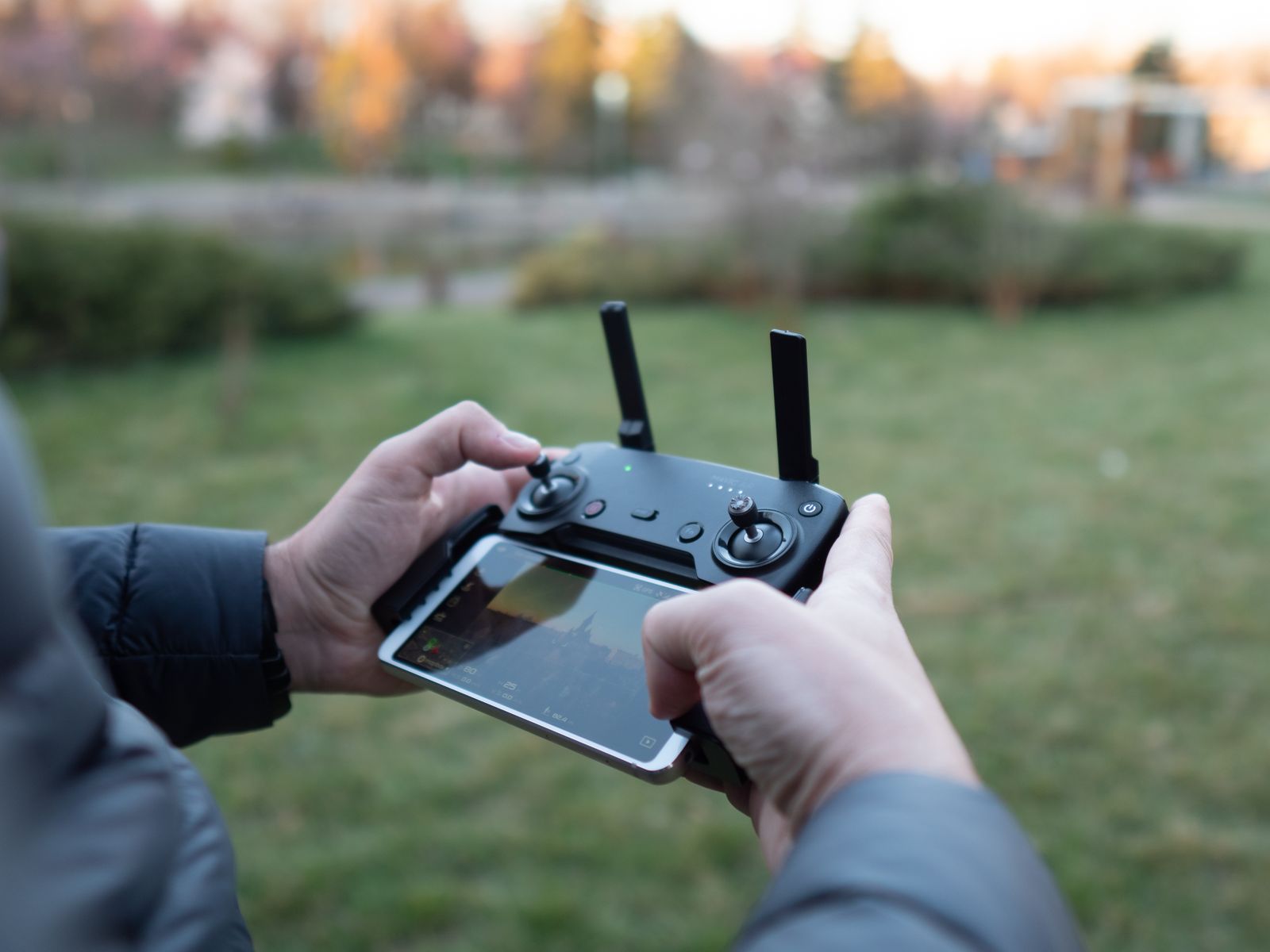 A pilot's hands on a drone controller in a park