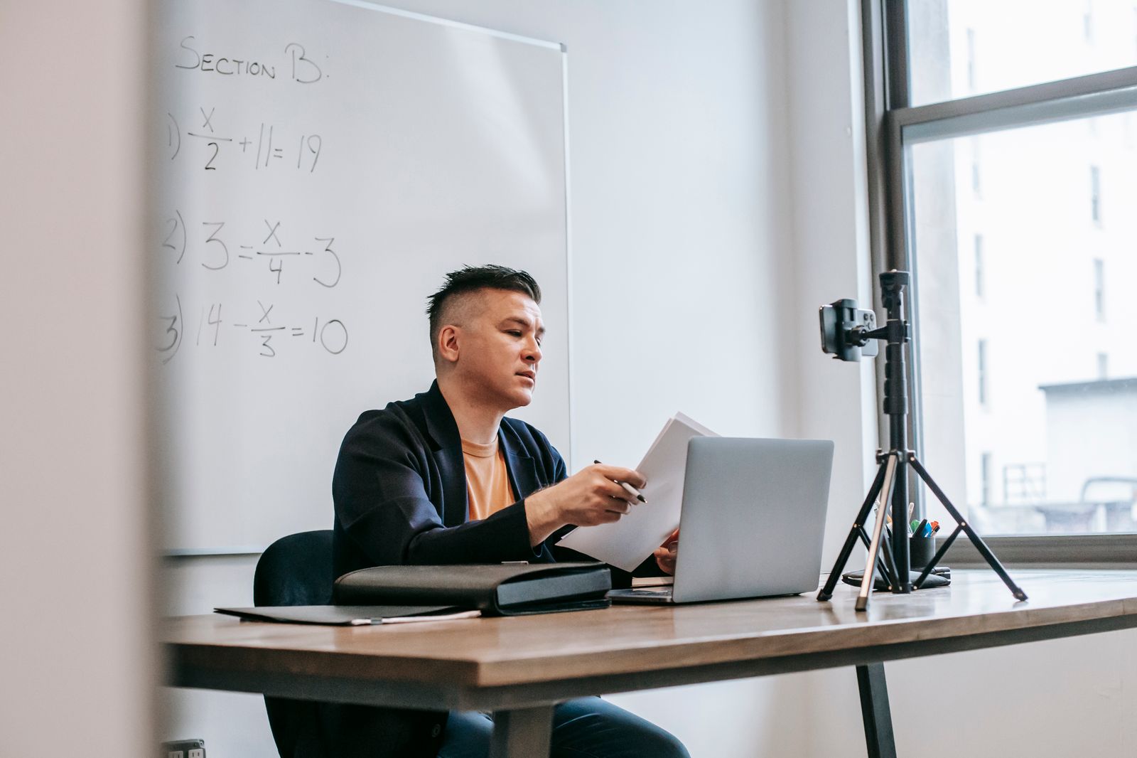 An instructor at a desk with a laptop and a camera on a tripod, recording a lesson