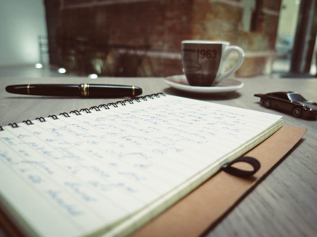 Handwritten notes, a fountain pen and a cup of coffee on a desk