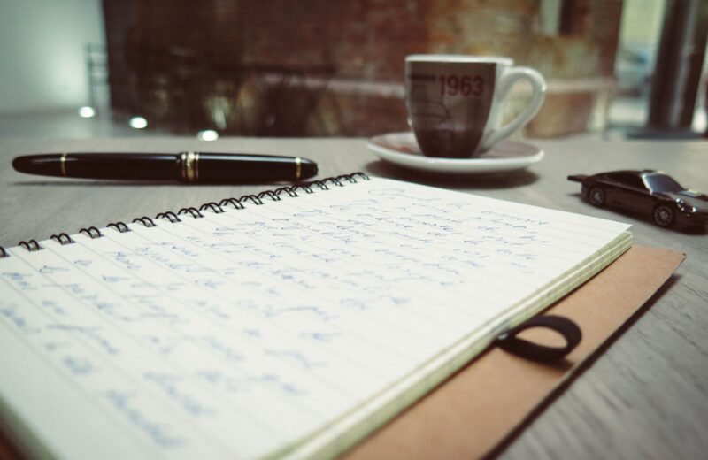 Handwritten notes, a fountain pen and a cup of coffee on a desk