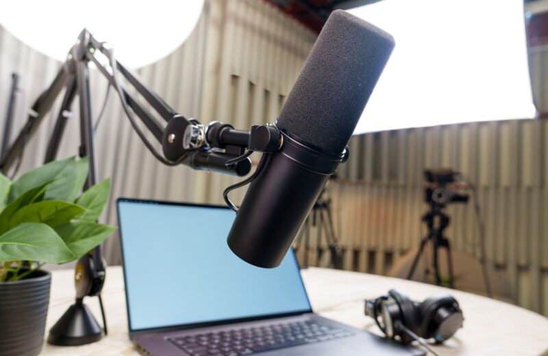 A microphone on an arm, a laptop and headphones set up for recording