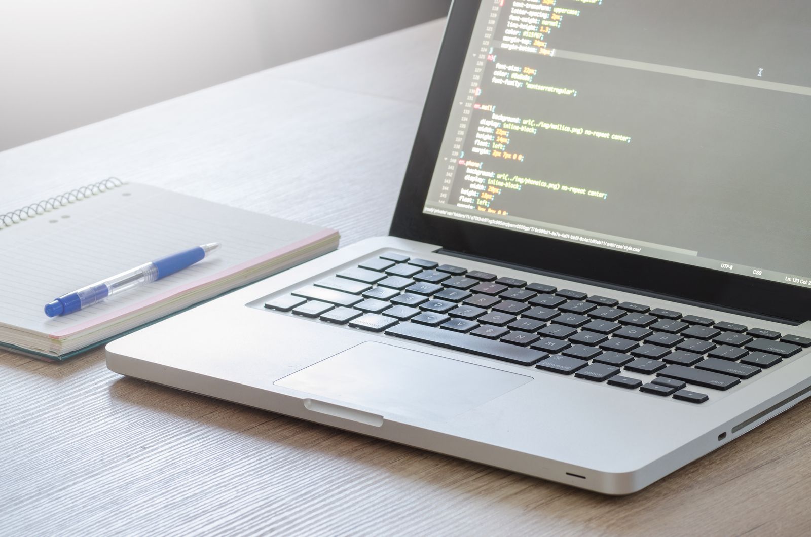 A laptop with a code editor open next to a notebook and pen