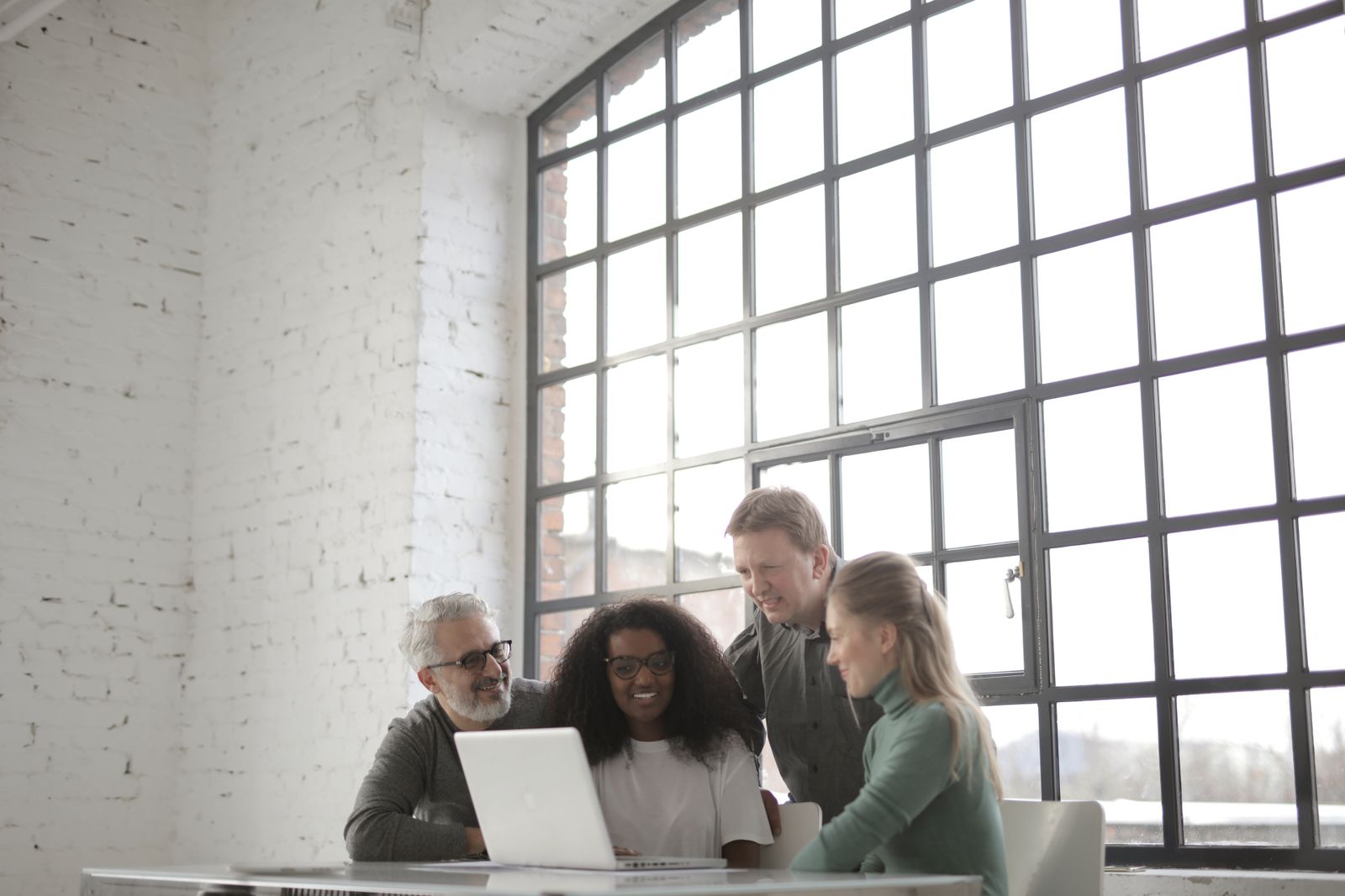 Four colleagues gathered round one laptop by a large window
