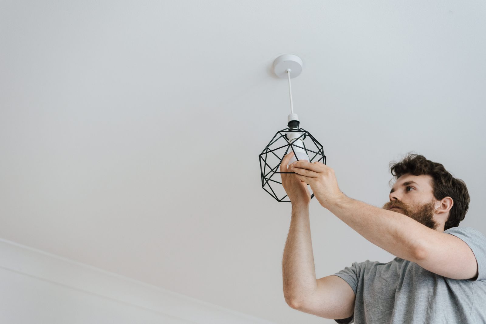 An electrician fitting a wire cage pendant light to a white ceiling