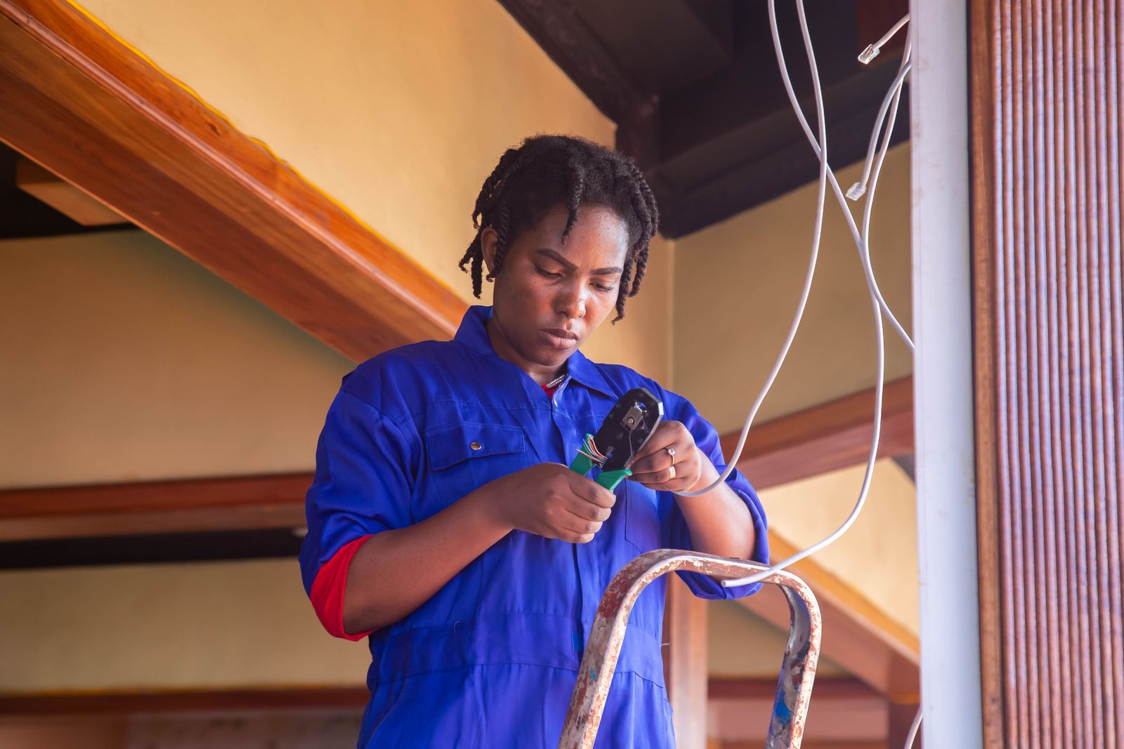 An electrician in blue overalls connecting wires at a wall during a renovation