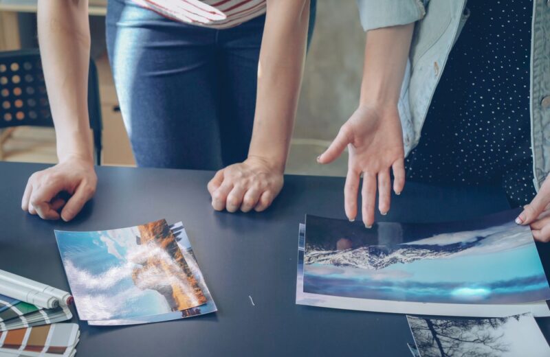 Hands pointing at large printed photographs on a dark table