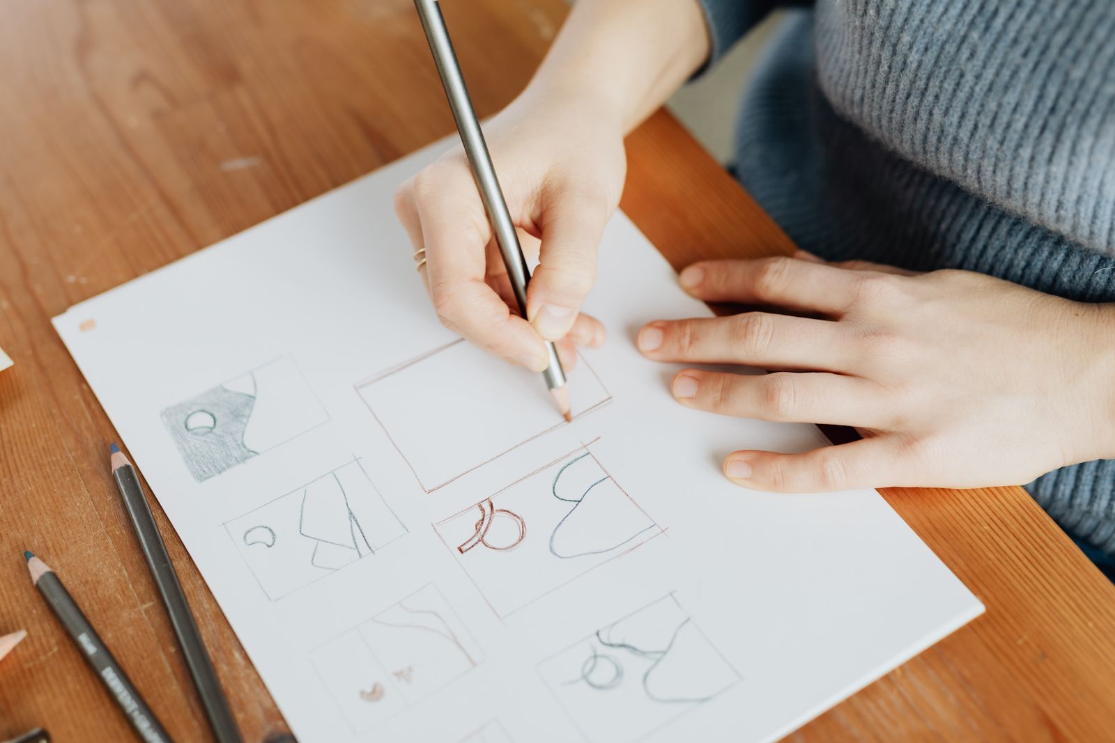A designer's hands sketching small marks in pencil on a sheet of paper