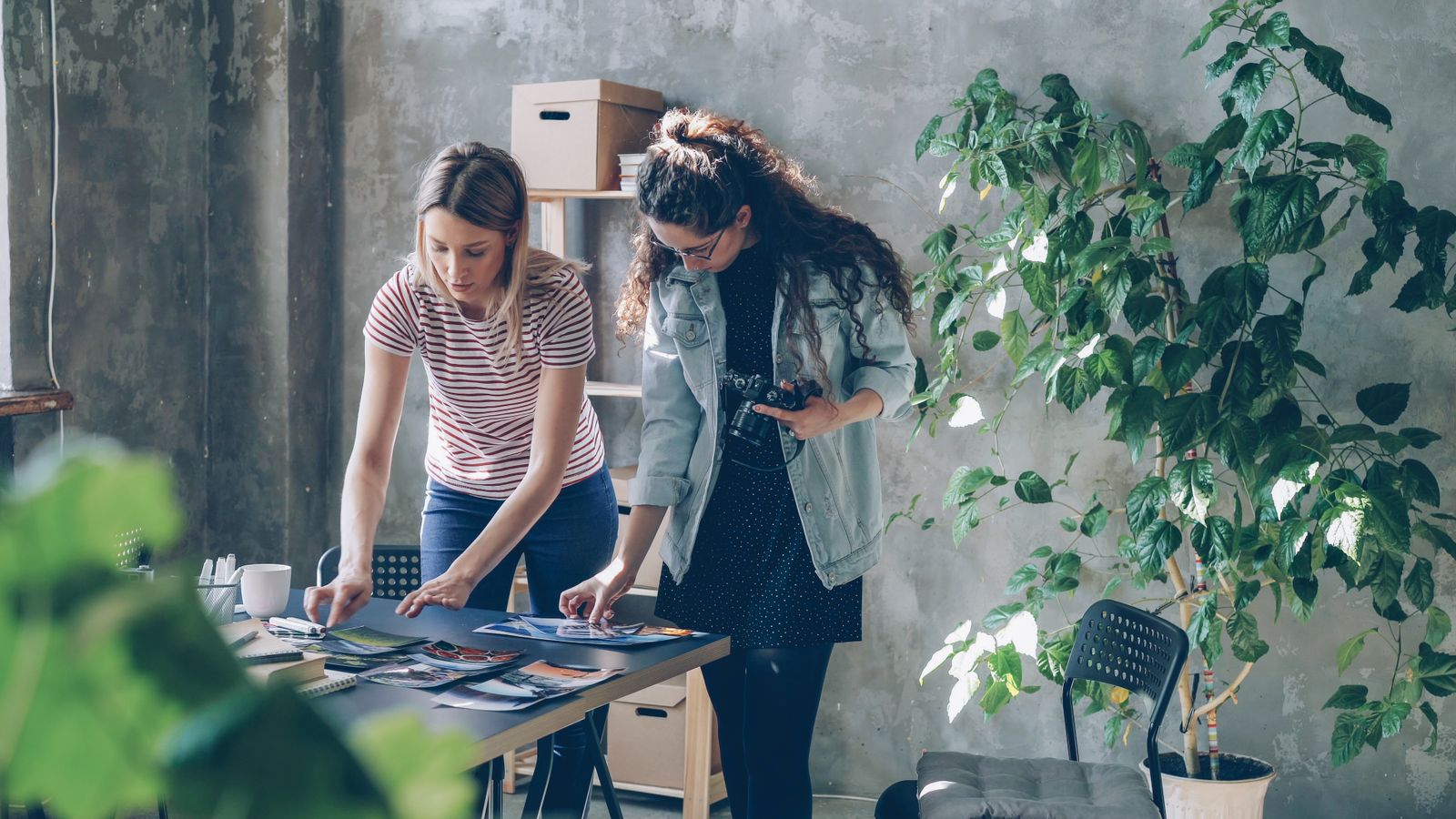 Two designers comparing printed proofs at a long table in a bright studio