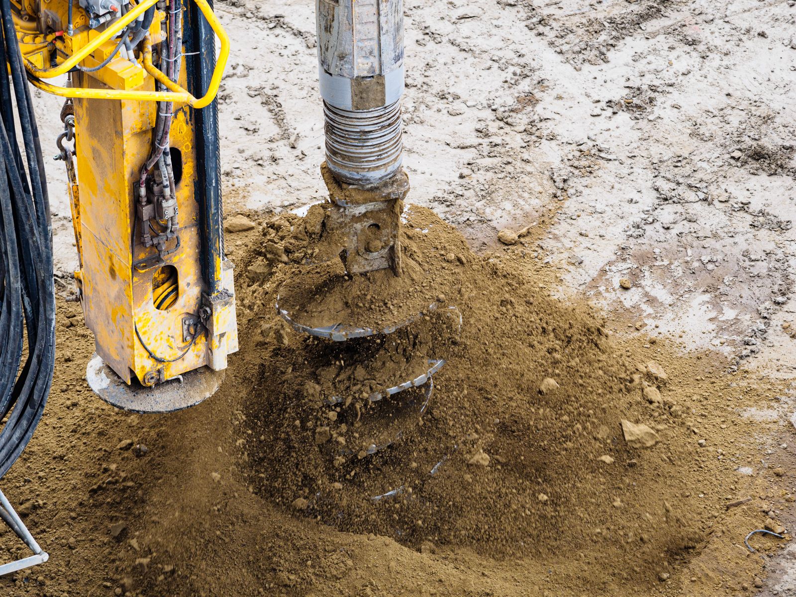 A drilling auger turning sandy soil out of a borehole