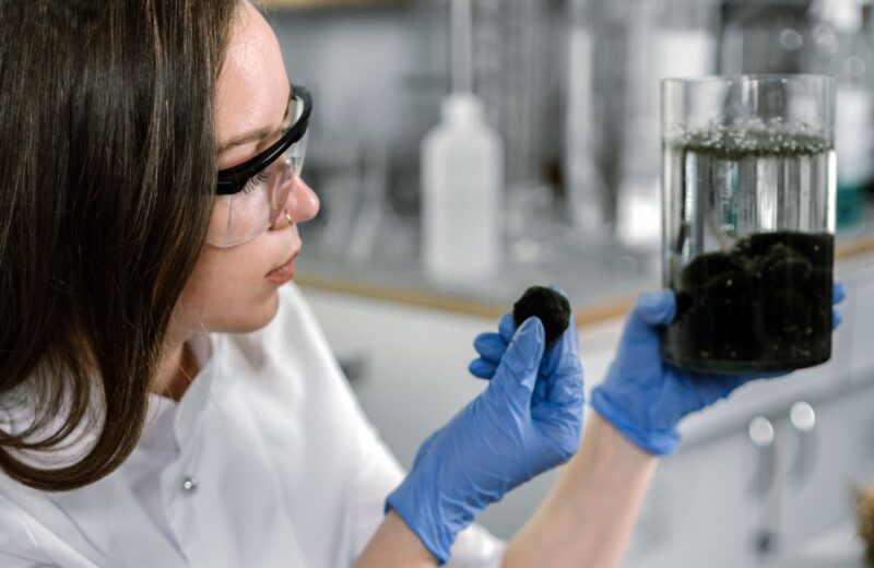 A lab analyst in gloves holding up a jar of soil and a soil sample