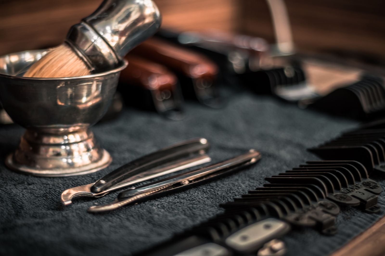 Straight razors, combs and a shaving brush in a steel bowl, laid out on a dark barber's cloth