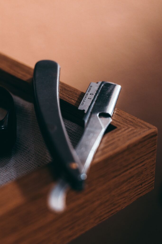 A straight razor with a dark handle resting open on the edge of a wooden box in warm light