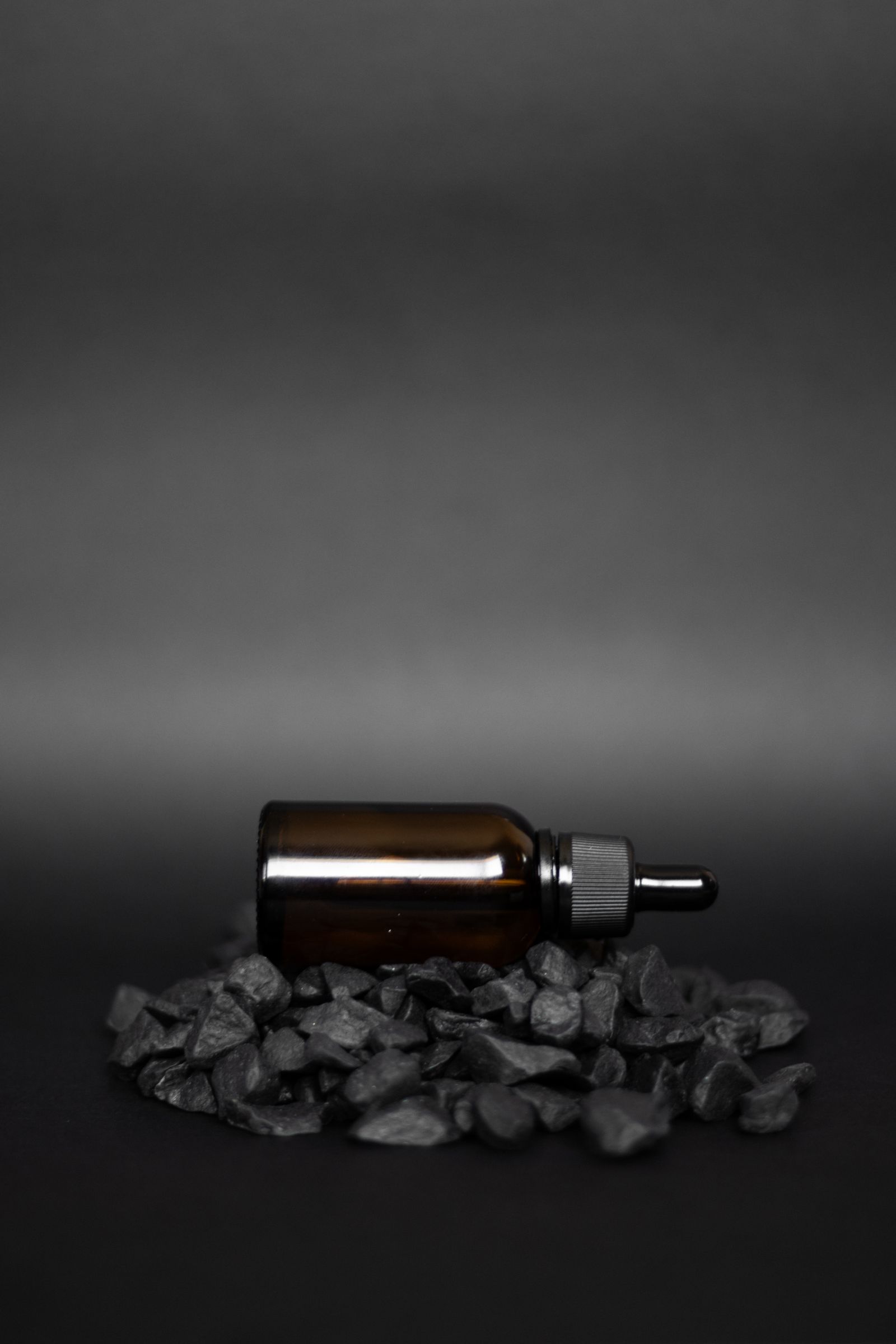 A small dark glass dropper bottle lying on black stones