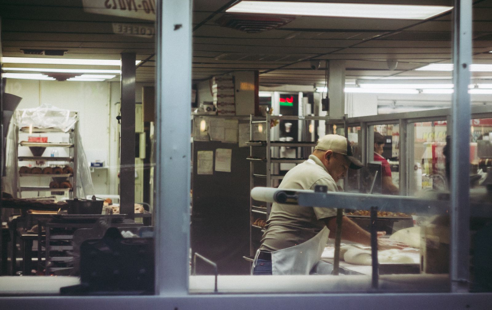 A baker working dough in a bakery kitchen, seen through the window before dawn
