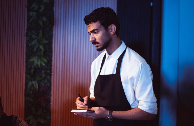 A waiter in an apron writing on a notepad in a restaurant