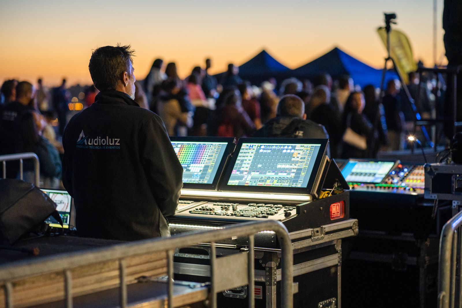 A technician at a sound and lighting desk behind the audience at an evening event
