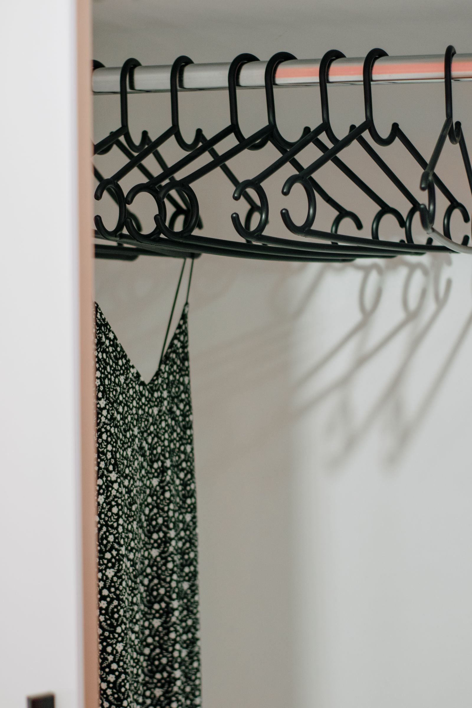 A patterned slip dress on a black hanger in a white wardrobe, its shadow on the wall