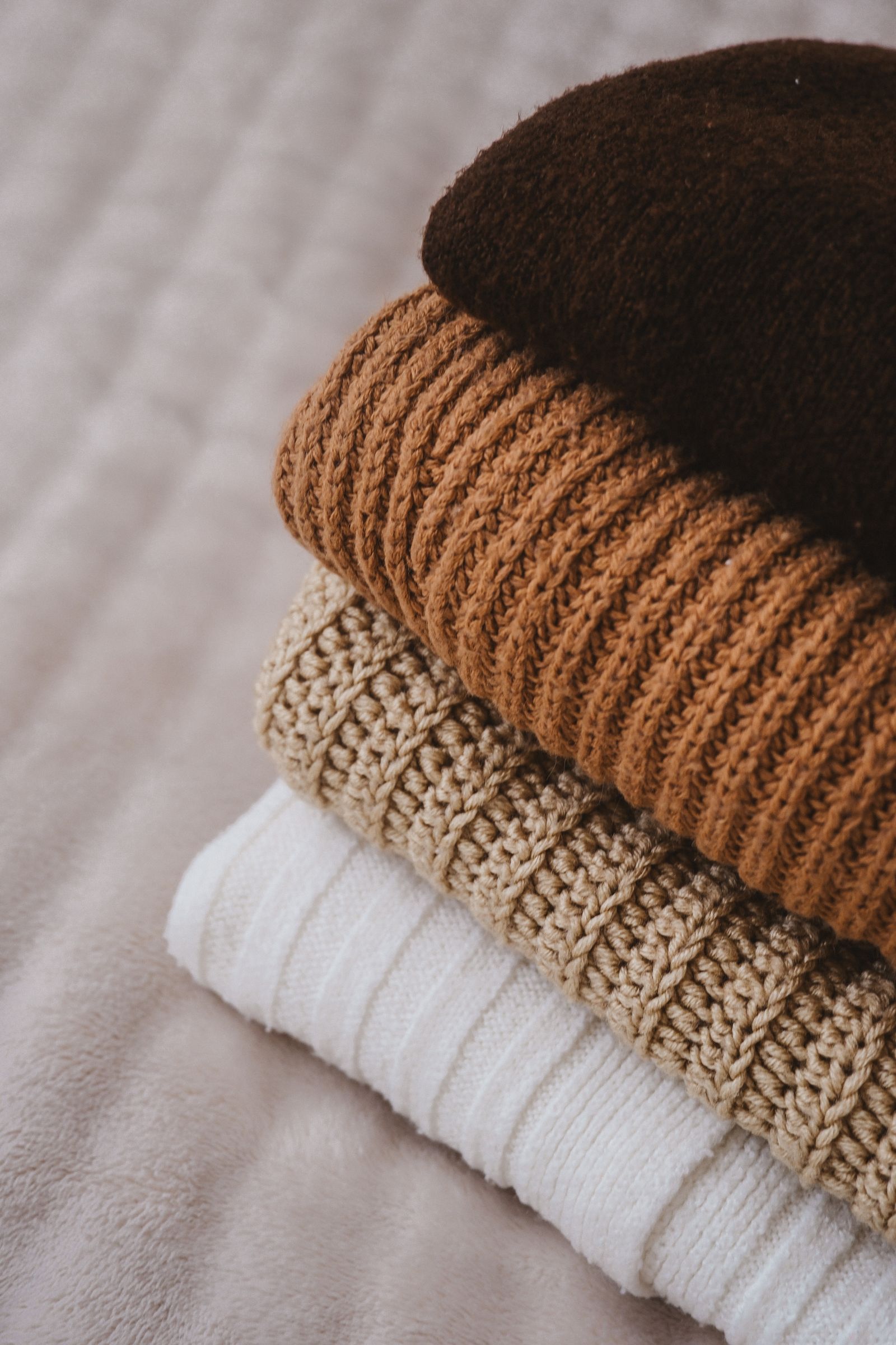 A stack of folded jumpers in rust, oat and white rib knits