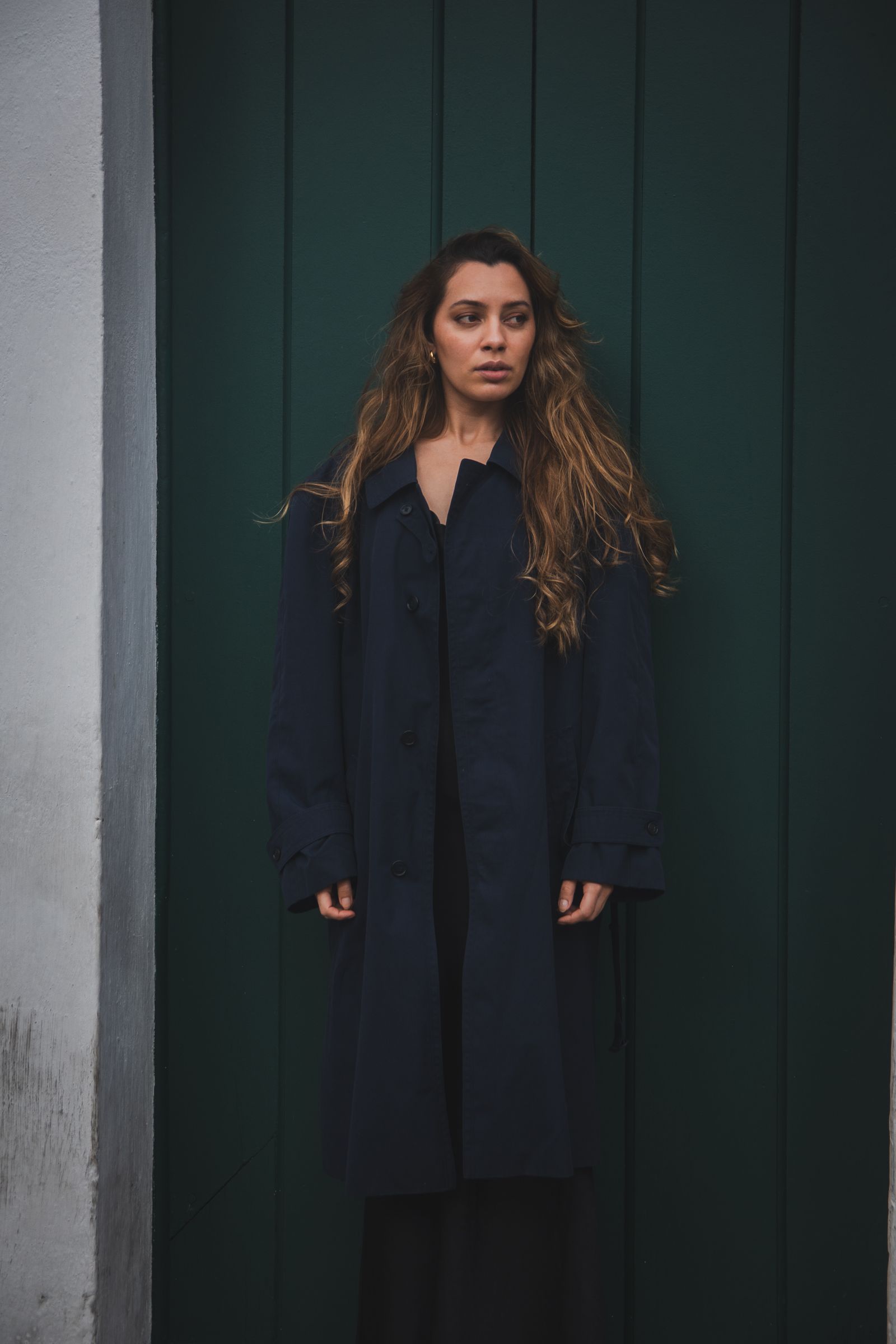 A woman in a long dark navy coat standing in front of a green wooden door