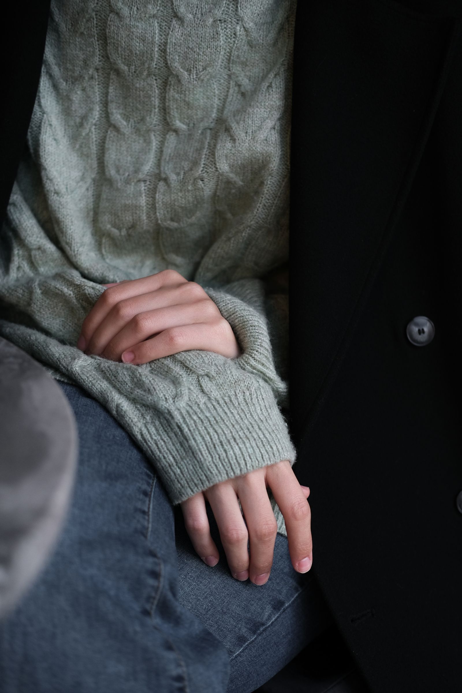Close-up of hands folded in the cuffs of a sage green cable-knit jumper