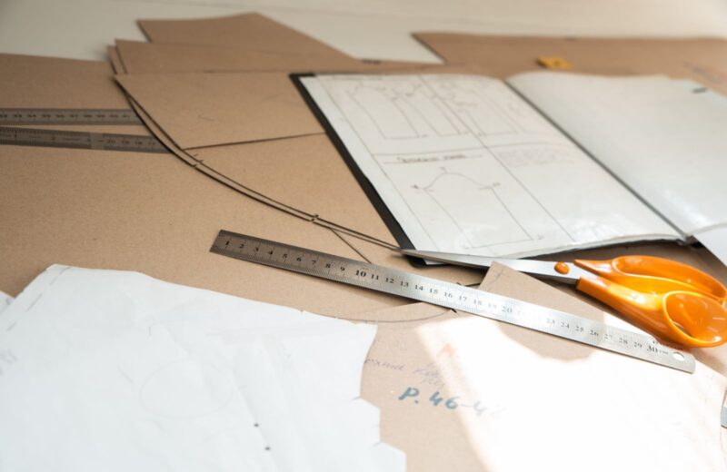 Paper patterns, a metal ruler and orange scissors on a cutting table
