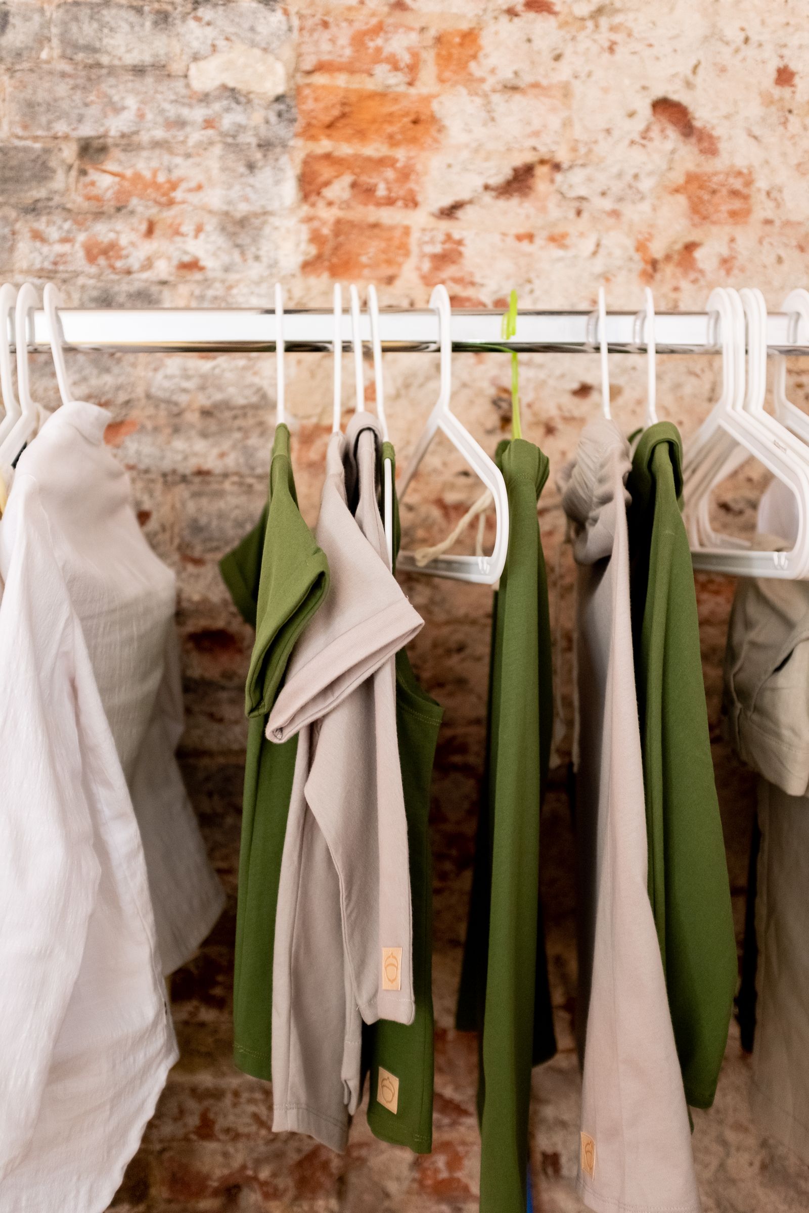 Green and white garments on hangers along a rail against a brick wall