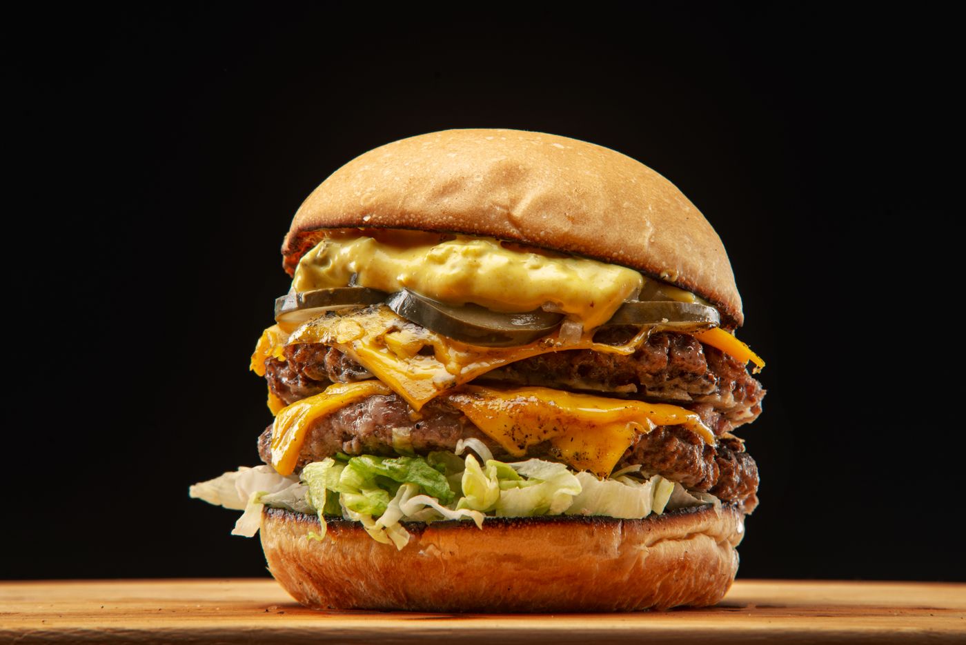 A tall cheeseburger with pickles, lettuce and melted cheese on a black background