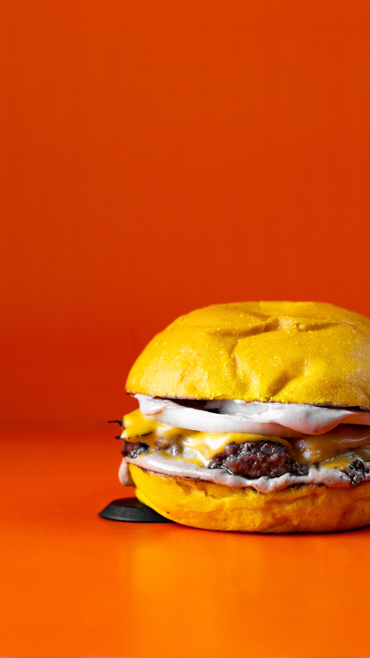 A cheeseburger with a golden bun and melted cheese against an orange background