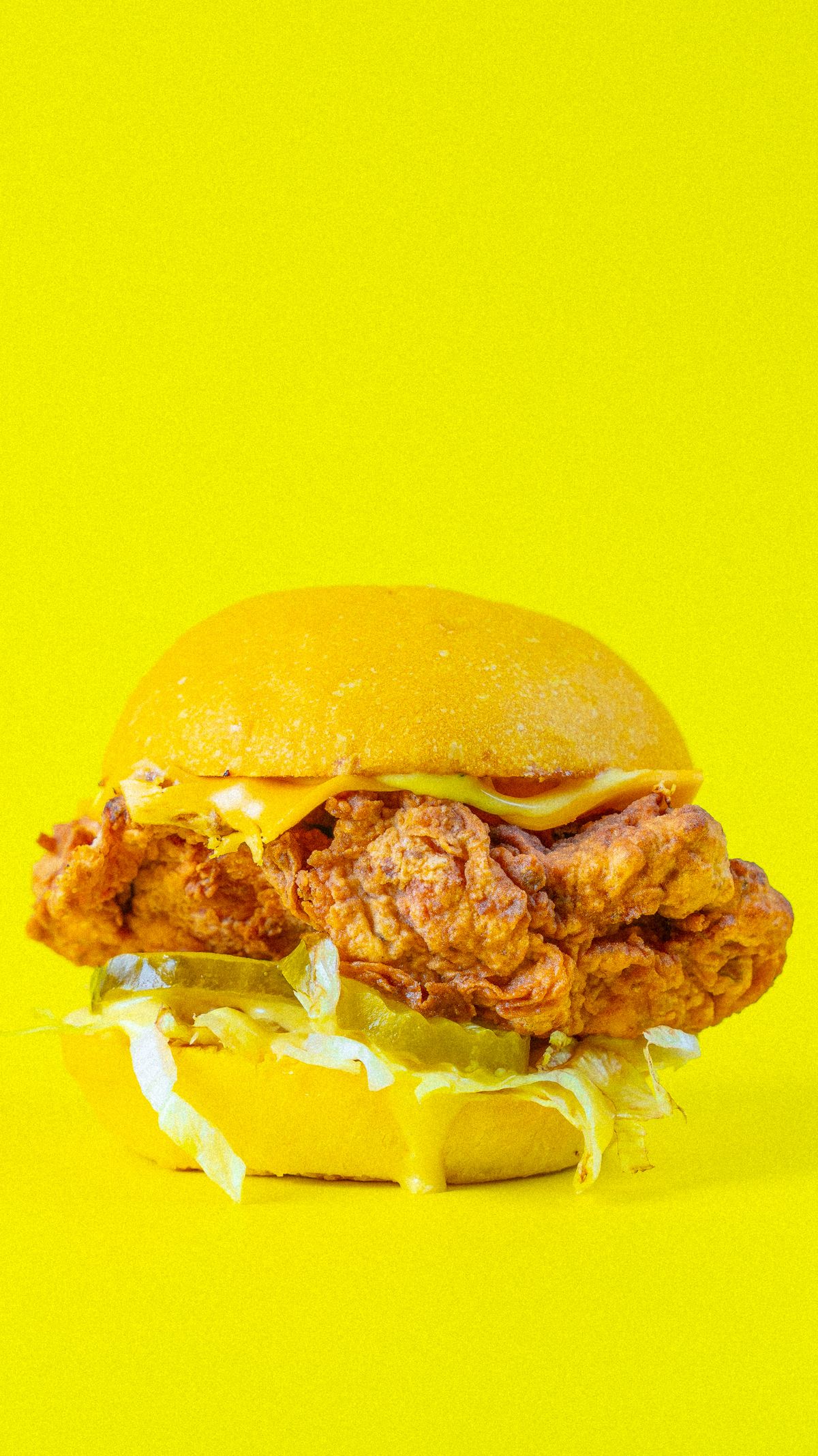 A crispy chicken burger with melted cheese and sauce on a bright yellow background