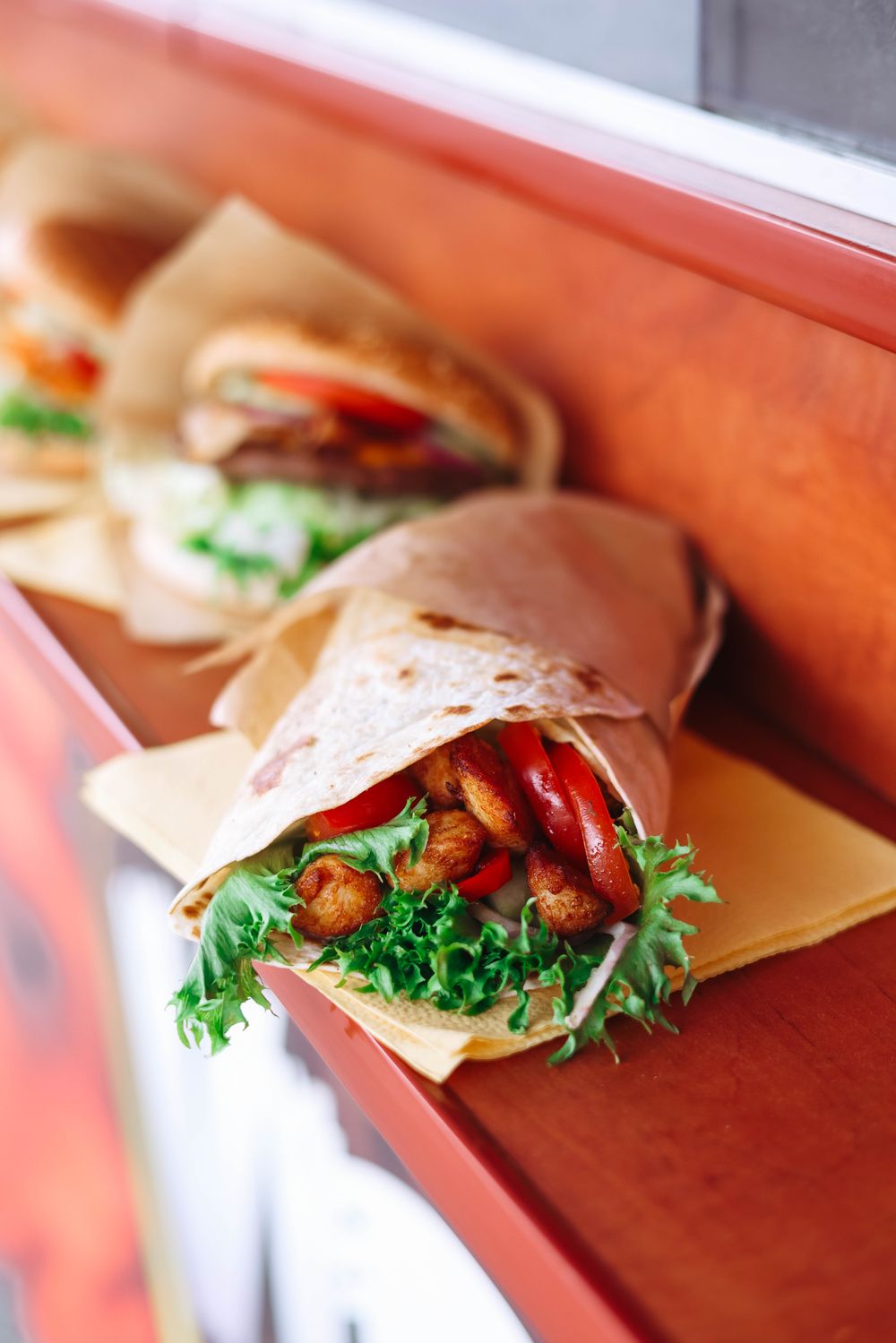 A tortilla wrap filled with crispy chicken, tomato and greens on an orange background