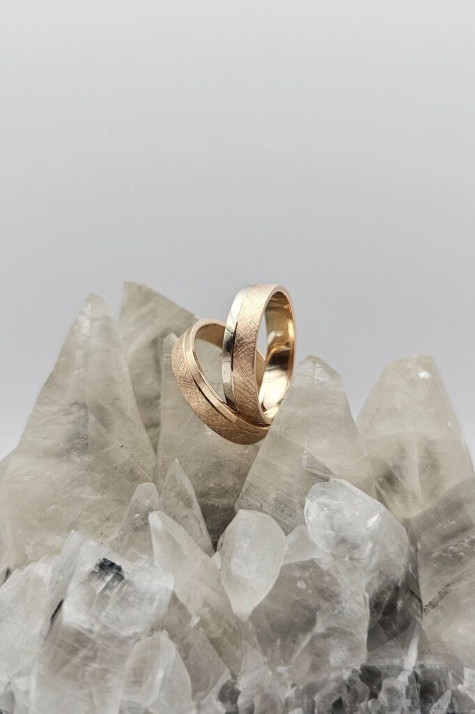 Two textured gold wedding bands, one rose and one yellow, standing on clear quartz