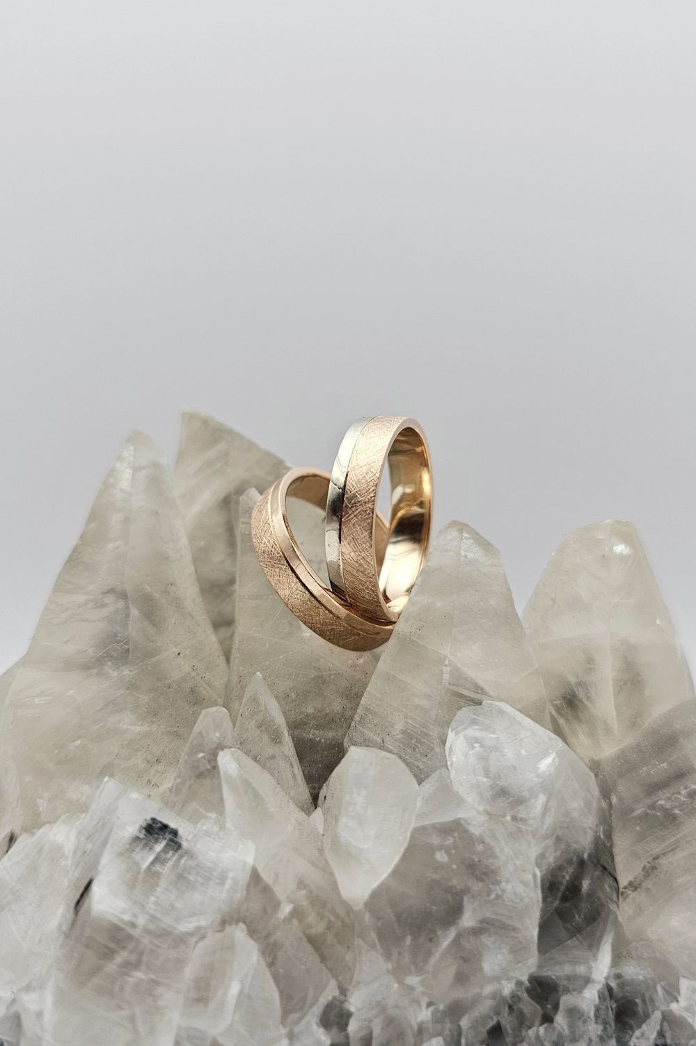 Two textured gold wedding bands, one rose and one yellow, standing on clear quartz