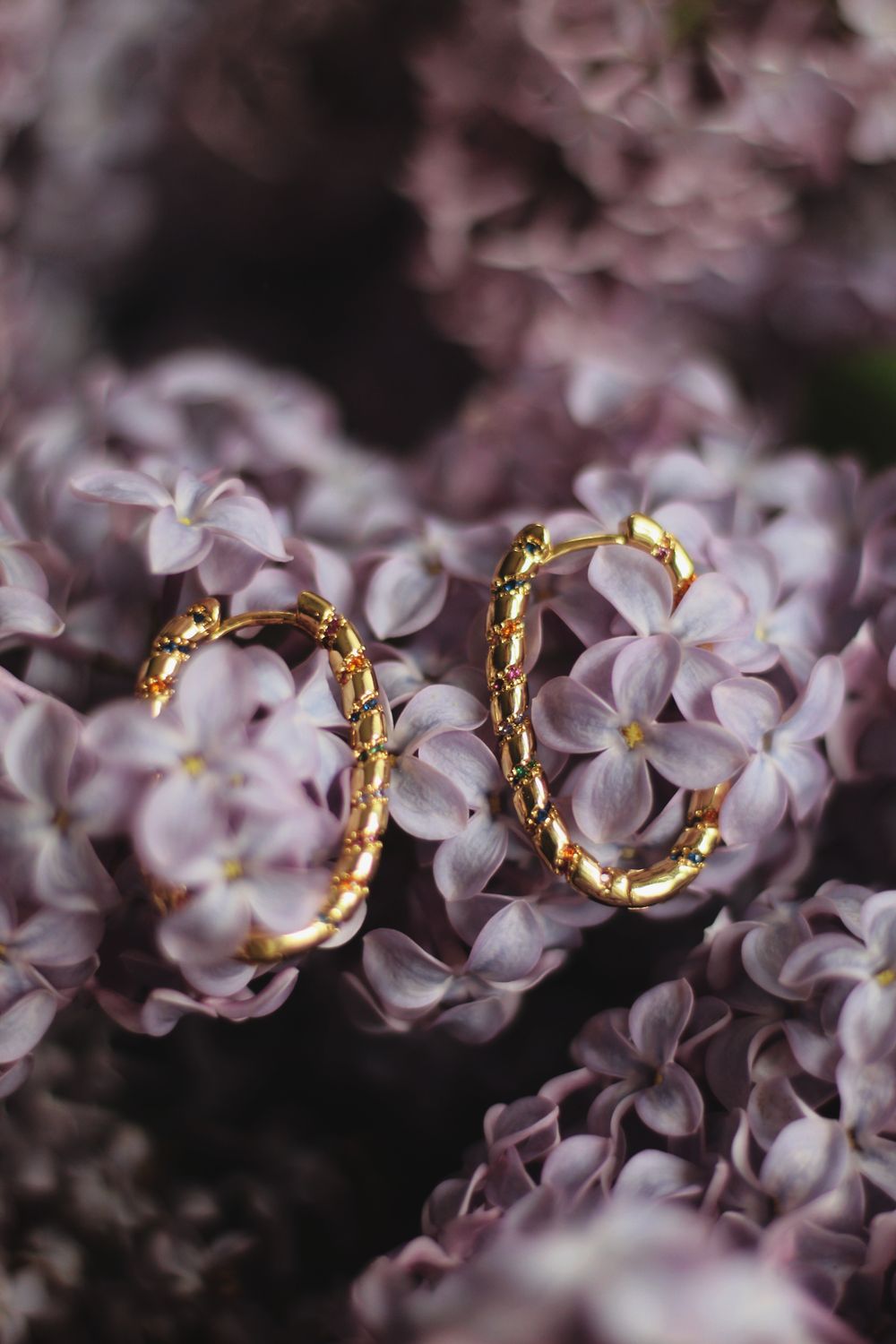 A pair of twisted gold hoop earrings resting on lilac blossom