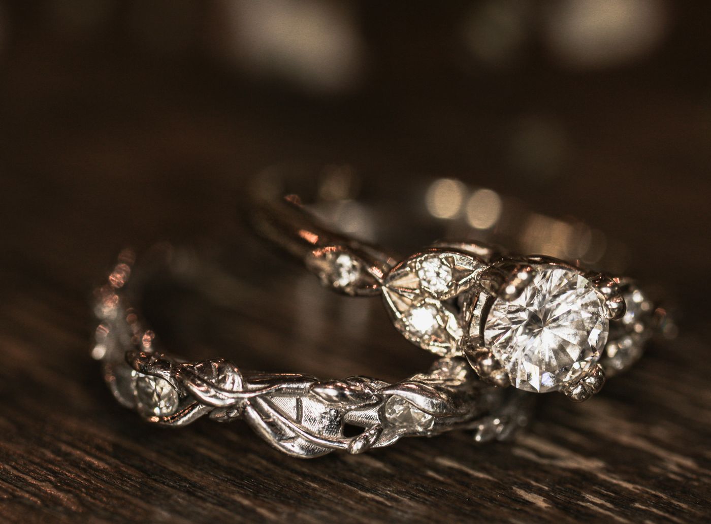 A diamond engagement ring and a matching band with leaf shoulders on dark wood