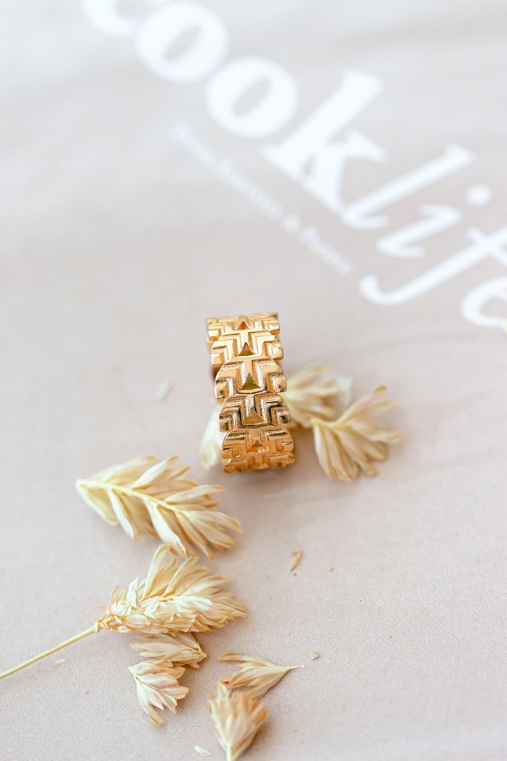 A wide gold ring with a woven basket pattern on linen beside dried wheat
