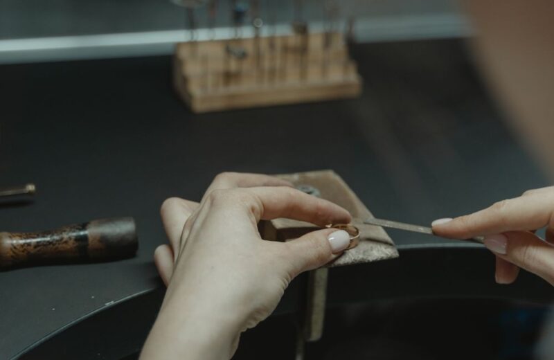 Hands filing a ring held against the bench peg in a jeweller's workshop